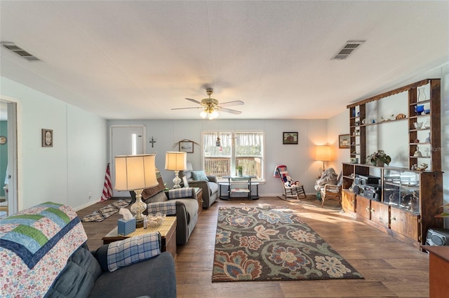 living room featuring a ceiling fan, visible vents, baseboards, and wood finished floors