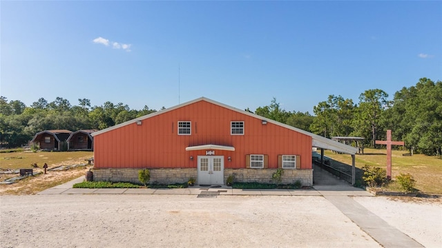 view of front facade featuring a carport, stone siding, concrete driveway, and french doors