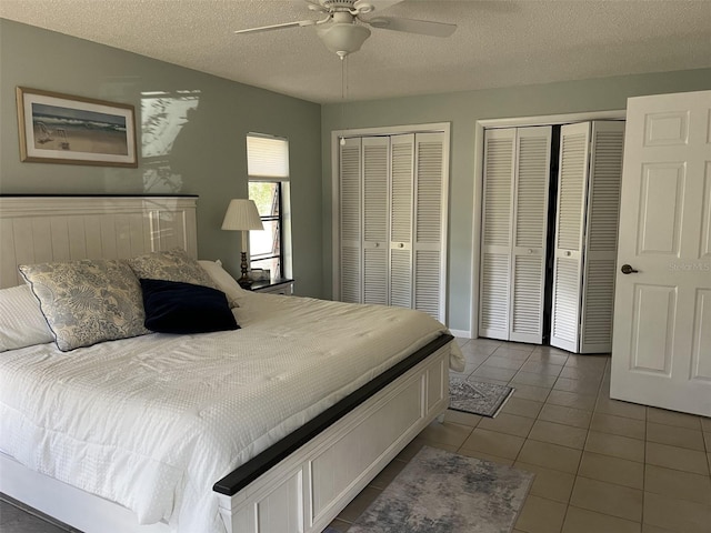 bedroom featuring dark tile patterned floors, a textured ceiling, a ceiling fan, and multiple closets