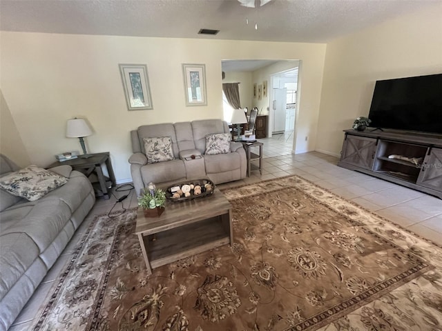 living area featuring a textured ceiling, light tile patterned floors, visible vents, and baseboards