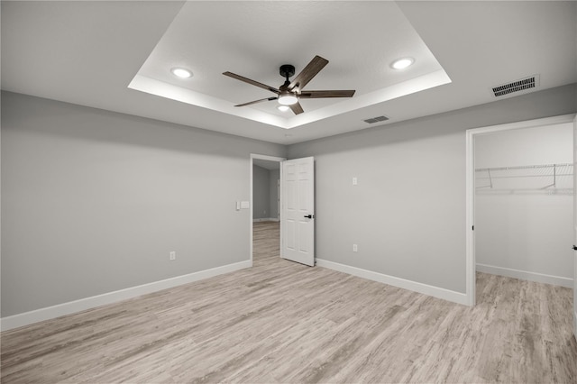 unfurnished bedroom featuring a raised ceiling, visible vents, light wood-style flooring, and baseboards