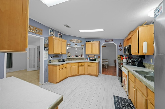 kitchen with range with electric stovetop, a sink, light countertops, light brown cabinetry, and stainless steel microwave