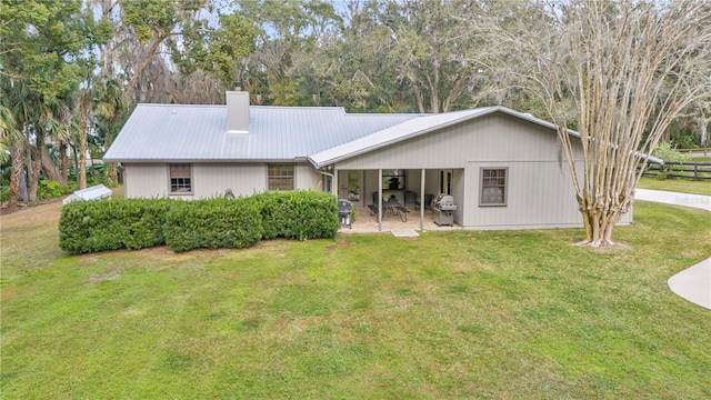 rear view of house with a patio area, a chimney, metal roof, and a yard