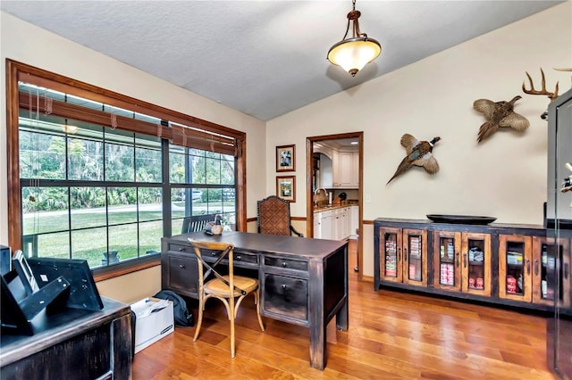 office area with light wood-type flooring, a textured ceiling, vaulted ceiling, and a sink