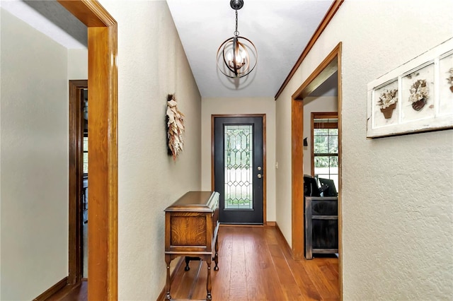 foyer with baseboards, a textured wall, wood-type flooring, and a notable chandelier