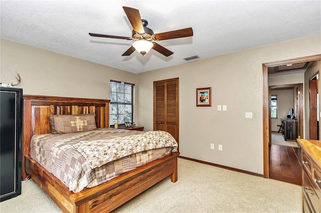 bedroom featuring baseboards, visible vents, light colored carpet, a textured ceiling, and a closet