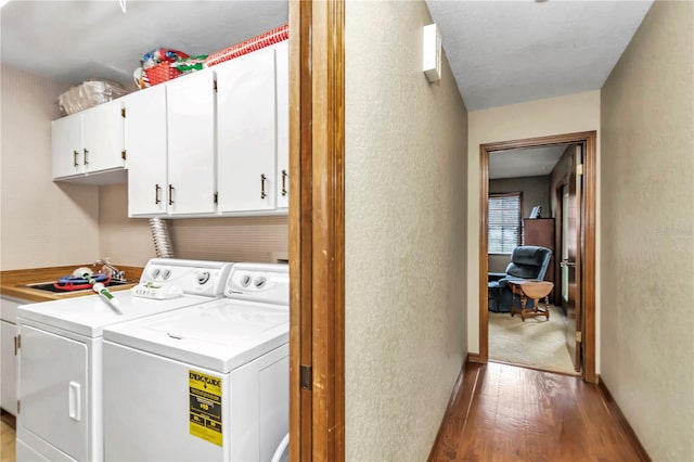 laundry area with cabinet space, baseboards, a textured wall, wood finished floors, and washing machine and dryer