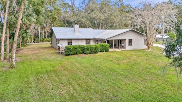 back of property with metal roof, a yard, and a chimney