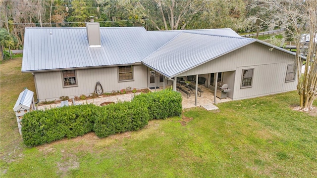 rear view of property with metal roof, a patio area, a lawn, and a chimney