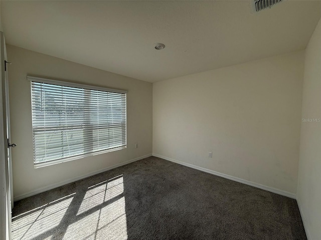 unfurnished room with dark colored carpet, visible vents, and baseboards