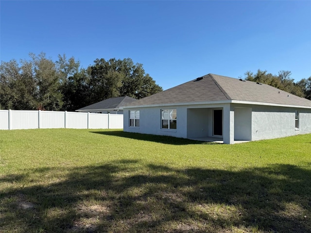 back of property featuring roof with shingles, fence, a lawn, and stucco siding