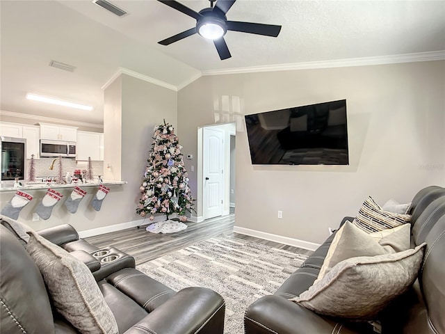 living area with crown molding, visible vents, vaulted ceiling, wood finished floors, and baseboards