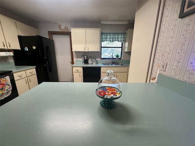 kitchen featuring light countertops, cream cabinets, a sink, black appliances, and wallpapered walls