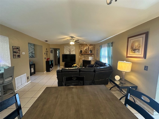 living room featuring visible vents, light tile patterned flooring, ceiling fan, a stone fireplace, and baseboards