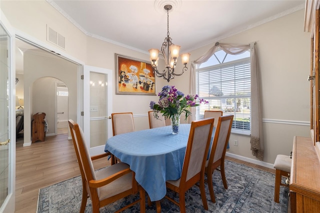 dining room with arched walkways, visible vents, baseboards, light wood finished floors, and crown molding