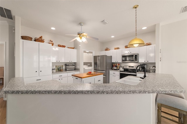 kitchen featuring a peninsula, a sink, visible vents, white cabinets, and appliances with stainless steel finishes