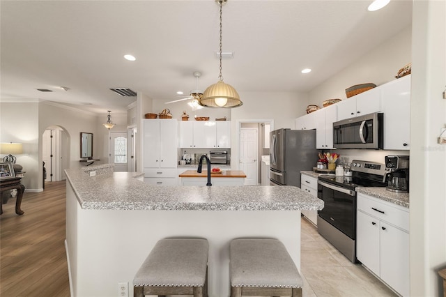 kitchen with arched walkways, pendant lighting, stainless steel appliances, visible vents, and an island with sink