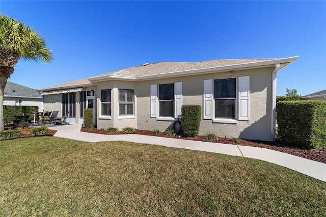 view of front of property featuring stucco siding, roof with shingles, a patio, and a front yard