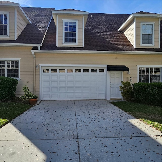 cape cod-style house featuring concrete driveway, roof with shingles, and an attached garage