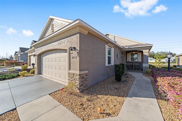 view of side of home featuring a garage, covered porch, stone siding, driveway, and stucco siding