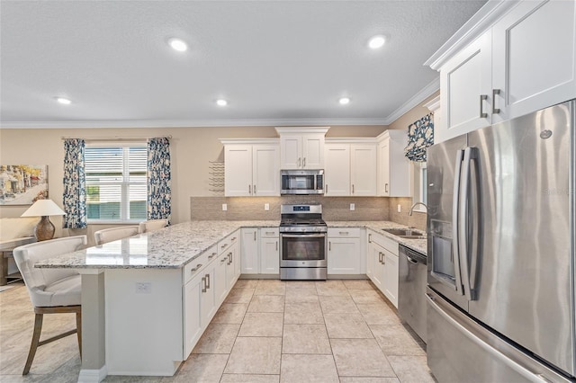 kitchen with appliances with stainless steel finishes, ornamental molding, white cabinets, a sink, and a kitchen bar