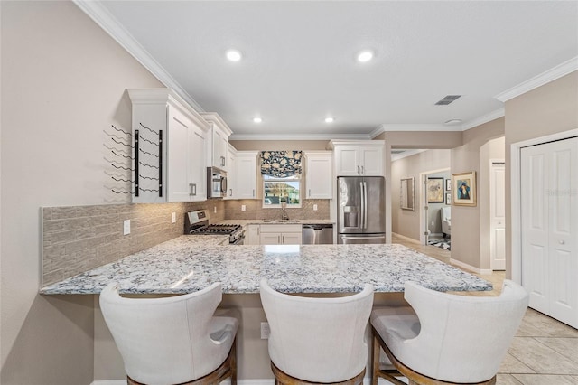 kitchen featuring visible vents, a kitchen breakfast bar, a peninsula, stainless steel appliances, and white cabinetry