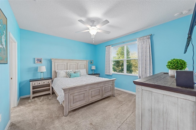 bedroom with ceiling fan, baseboards, a textured ceiling, and light colored carpet