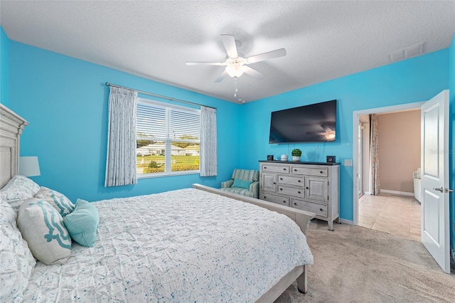 bedroom with baseboards, visible vents, light colored carpet, ceiling fan, and a textured ceiling