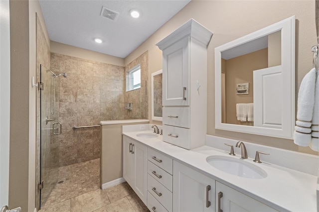 full bathroom with double vanity, a shower stall, visible vents, and a sink