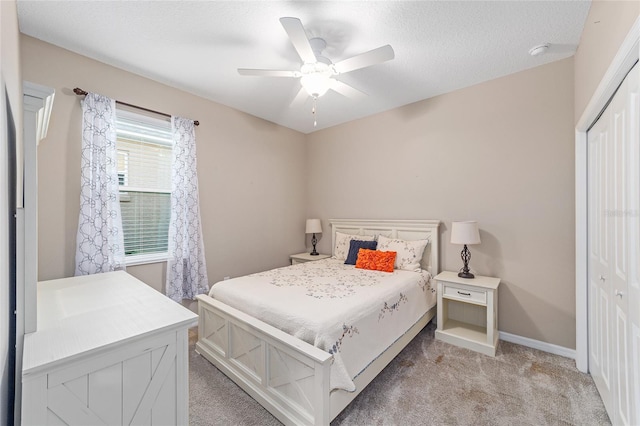 bedroom featuring baseboards, a ceiling fan, light colored carpet, a textured ceiling, and a closet