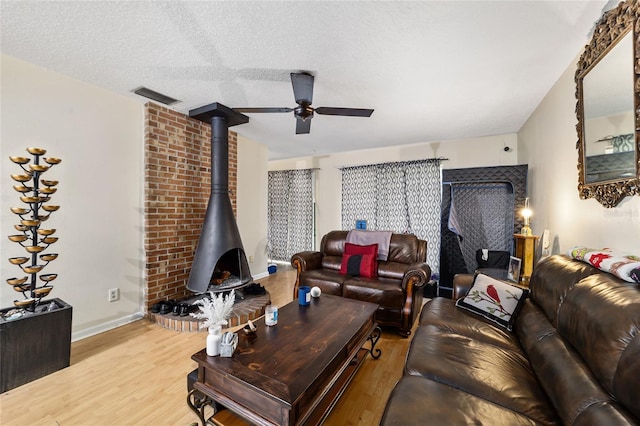 living room with light wood finished floors, baseboards, visible vents, a wood stove, and a textured ceiling