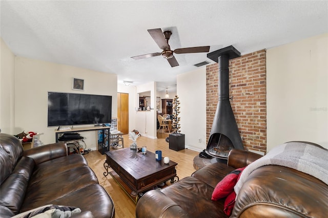 living area featuring a textured ceiling, light wood-style flooring, a wood stove, and a ceiling fan