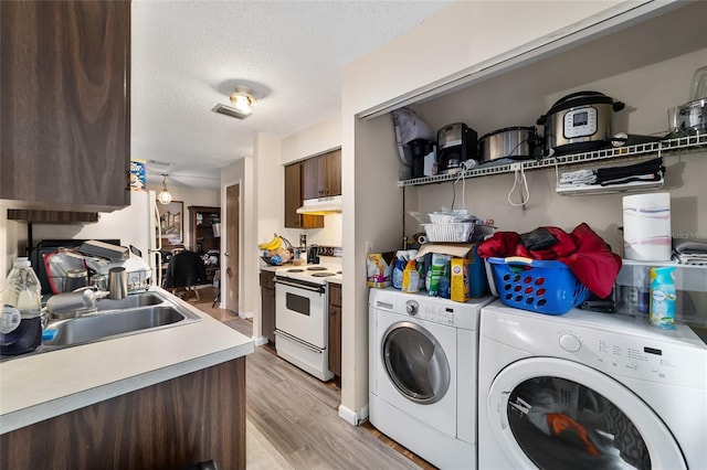 laundry area with a textured ceiling, light wood finished floors, washer and clothes dryer, and a sink