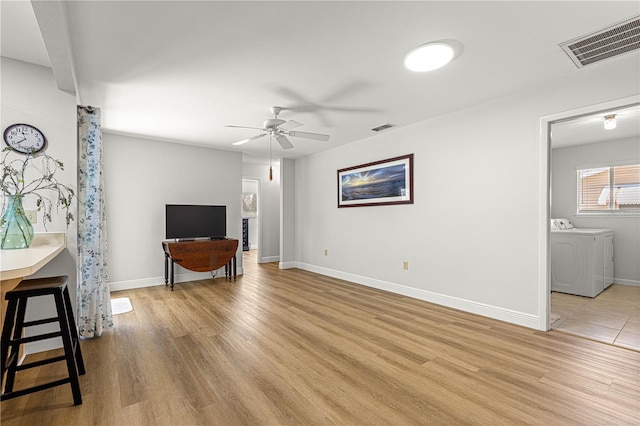 living room featuring light wood-type flooring, visible vents, a ceiling fan, and independent washer and dryer