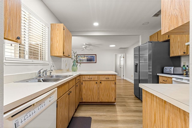 kitchen with a peninsula, white appliances, a sink, light countertops, and light wood finished floors