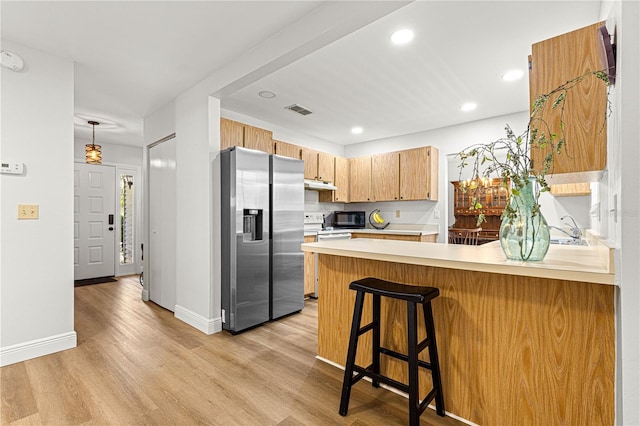 kitchen with black microwave, a peninsula, visible vents, light countertops, and stainless steel fridge