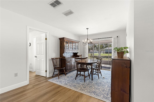 dining space with baseboards, wood finished floors, visible vents, and an inviting chandelier