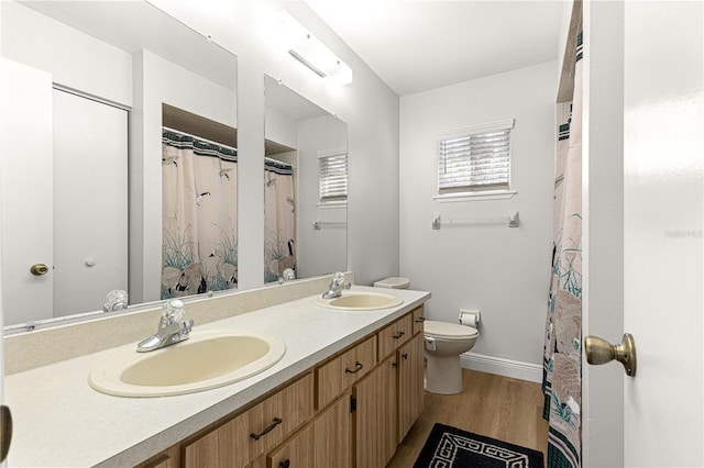 bathroom with double vanity, a sink, toilet, and wood finished floors