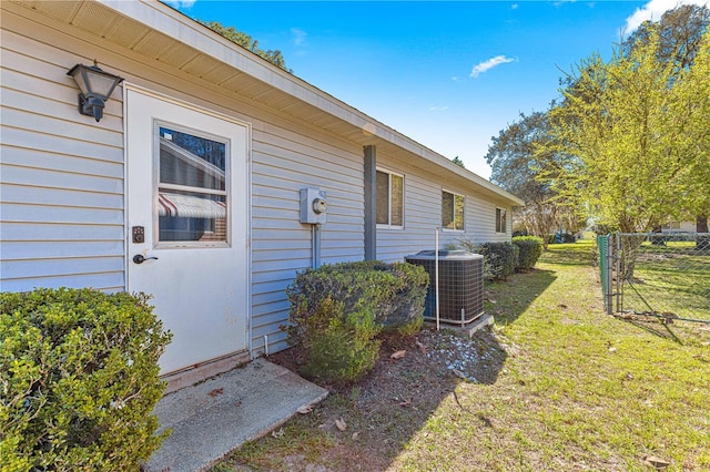 view of exterior entry with central AC unit, a lawn, and fence