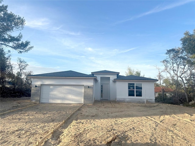 view of front of property featuring dirt driveway, an attached garage, and stucco siding