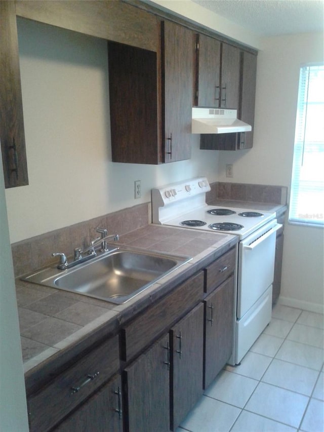 kitchen featuring light tile patterned flooring, dark brown cabinetry, under cabinet range hood, a sink, and white range with electric cooktop