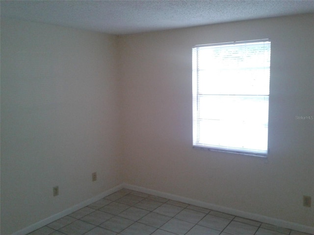 spare room with a textured ceiling, light tile patterned flooring, and baseboards