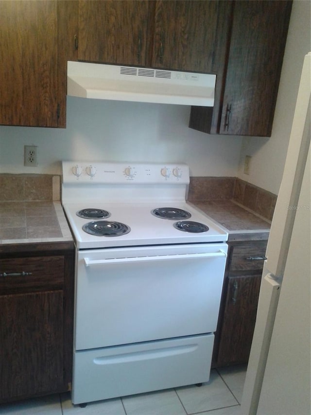 kitchen featuring light tile patterned floors, white appliances, dark brown cabinetry, and under cabinet range hood