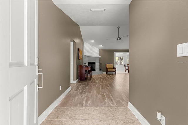 corridor with light tile patterned floors, baseboards, and vaulted ceiling