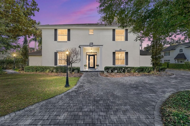 colonial home with fence, a front lawn, and stucco siding