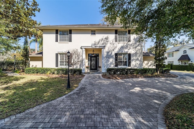 colonial inspired home with fence, a front lawn, and stucco siding