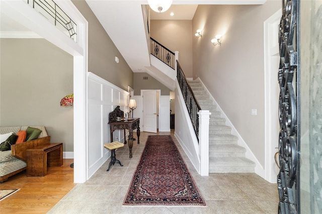 foyer with a high ceiling, visible vents, baseboards, stairs, and light wood finished floors