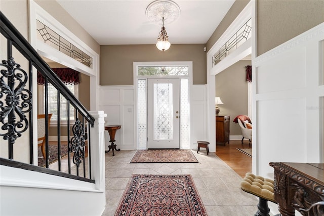 entrance foyer with a wealth of natural light, a wainscoted wall, a decorative wall, and light tile patterned floors