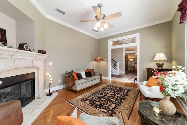 living area featuring crown molding, visible vents, stairway, a tiled fireplace, and wood finished floors