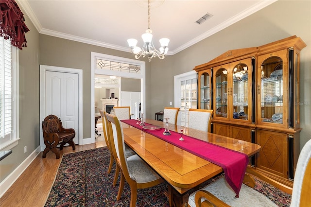 dining area featuring light wood finished floors, baseboards, visible vents, ornamental molding, and a fireplace